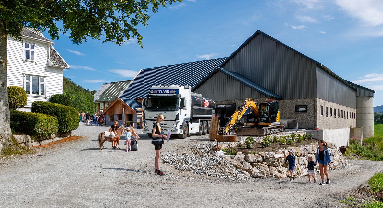 Liten hest foran låven på Solheim Gard i Sandnes, med melkebil og familier på vei inn på tunet.