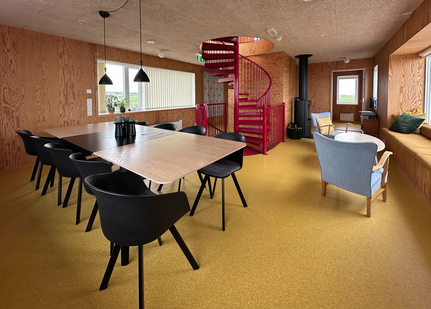 Langbord med stoler i stua i assistentboligen, med rød vindeltrapp, vedovn og vindusbenk.